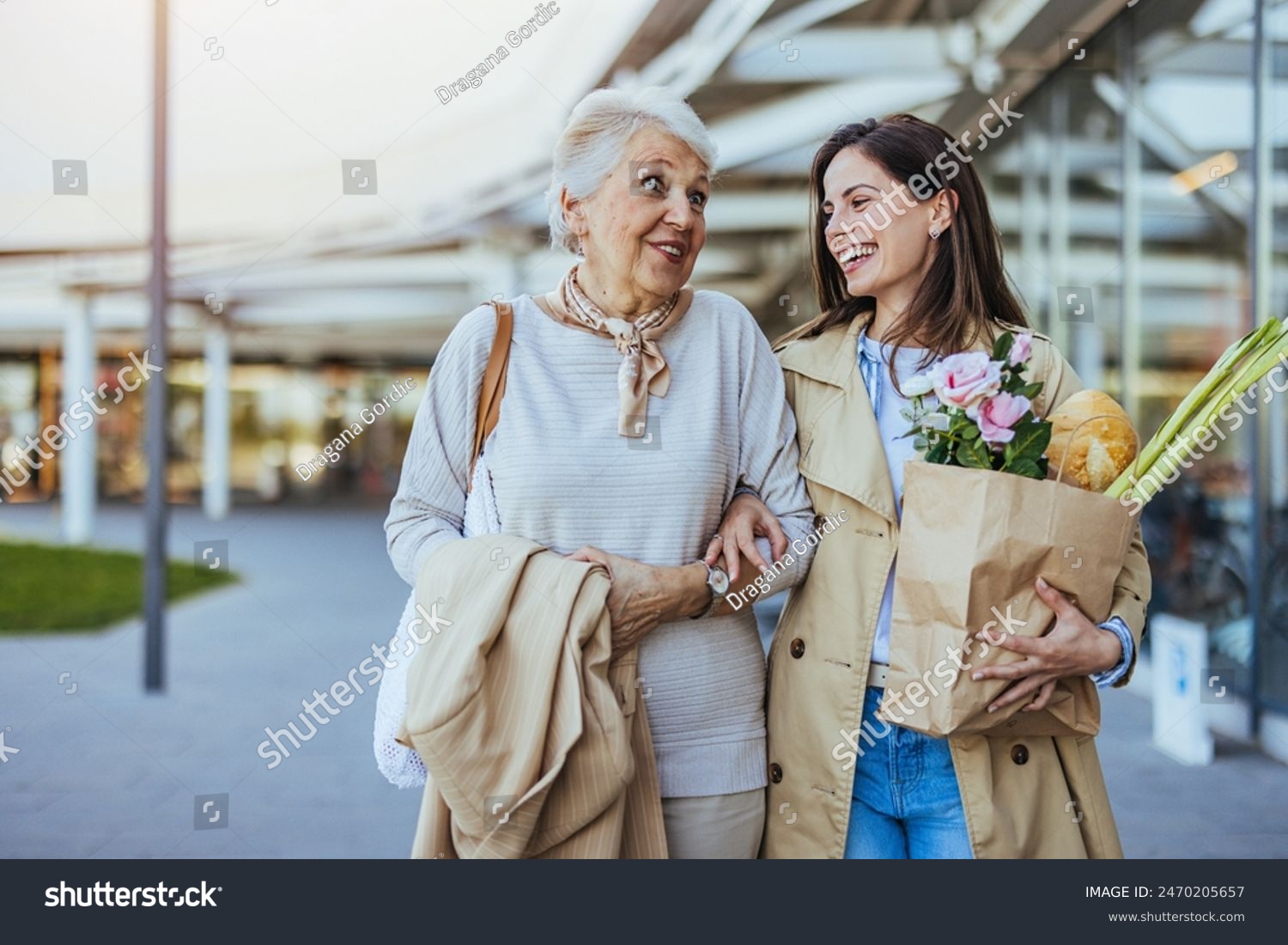 stock-photo-a-smiling-adult-woman-supports-her-senior-mother-laden-with-grocery-bags-outside-a-store-conveying-2470205657